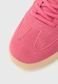 Κοντινό πλάνο στη μύτη ροζ σουέτ αθλητικού παπουτσιού με ροζ κορδόνια που ταιριάζουν και μπεζ λαστιχένια σόλα σε λευκό φόντο.