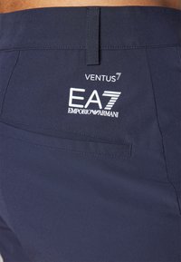 Σπορ σορτς σε ναυτικό μπλε χρώμα, κατασκευασμένα από ελαφρύ υλικό, με πίσω τσέπη και λογότυπο "VENTUS7 EA7 EMPORIO ARMANI" εκτυπωμένο σε λευκό χρώμα.