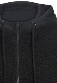 Schwarze Fleecejacke mit Reißverschluss, verfügt über eine strukturierte Außenseite, verstellbare Kordeln und ein glattes Innenfutter.