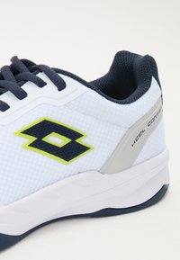 Bílé sportovní tenisky s texturovaným svrškem, námořnickými akcenty, fluorescenčním logem a šedým opěrka paty označenou jako "HEEL CONTROL."