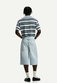 Polo a righe con maniche corte di colore azzurro chiaro e righe navy, abbinato a pantaloncini di jeans chiari con vestibilità rilassata e tasche posteriori.