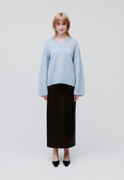 Light blue oversized knit sweater with ribbed hem, paired with a dark brown leather midi skirt and black pointed toe heels.