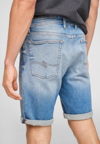 Vaaleansiniset farkkushortsit, joissa on käänteet, takataskut ompeluyksityiskohdilla ja normaali istuvuus. Pehmeä kangas.