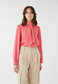 Koralfarvet bluse med halsbånd, lange puffede ærmer og glat stof, parret med beige skræddersyede bukser med cargo-lommer og folder.