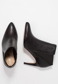 Botas de cuero negras hasta el tobillo con punta afilada, tacón de aguja y panel de tela elástica en el costado. Textura suave con acentos mínimos.