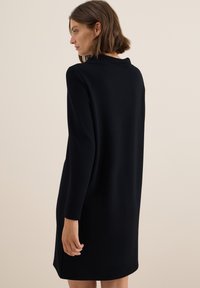 Svart, långärmad klänning, knä-lång, tillverkad av slätt tyg, med en subtil krage och avslappnad passform. Minimalistisk design utan mönster.