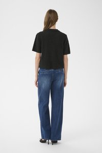 Črno teksturirano majico s kratkimi rokavi, združeno z modrimi širokimi kavbojkami z visokim pasom, ki imajo zadnje žepe in obrobe z raztrganim zaključkom.