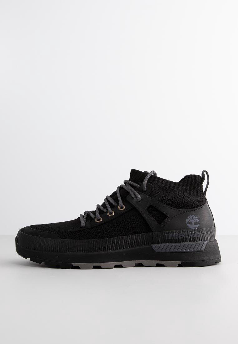 Baskets montantes noires avec empeigne en tissu tricoté, lacets gris, semelle épaisse et logo Timberland sur le côté et la languette du talon.