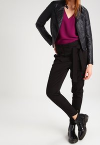 Chaqueta de cuero negra sobre una blusa morada, combinada con pantalones negros ajustados que tienen un cinturón atado, y botas negras brillantes hasta el tobillo.