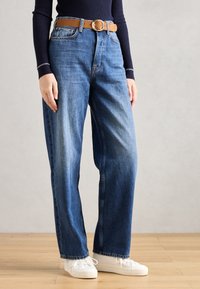 Lyseblå high-waisted jeans med en avslappet passform, med et brunt skinnbelte, noe bleking og rett ben-design. Hvite sneakers.
