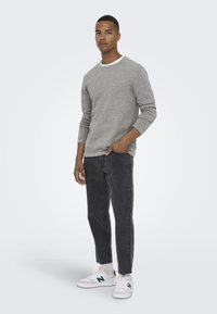 Camicetta grigia chiara a maniche lunghe con colletto bianco, abbinata a jeans neri a gamba asciutta e sneakers bianche con dettagli verdi.