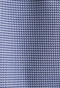 Primo piano di un tessuto a scacchi blu navy e bianco con piccole forme geometriche disposte in un modello ripetitivo.