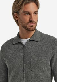 Grauer Reißverschluss-Pullover aus strukturiertem Stoff mit einem Kragen und einer Brusttasche, ausgestattet mit einem glatten Reißverschluss und sauberen Nähdetails.