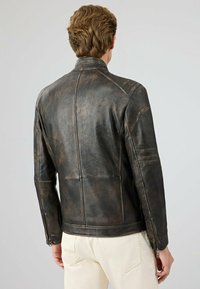 Bruine leren jas met een getailleerd ontwerp, gladde textuur, staande kraag en ritsmanchetten met subtiele matte afwerkingsdetails.