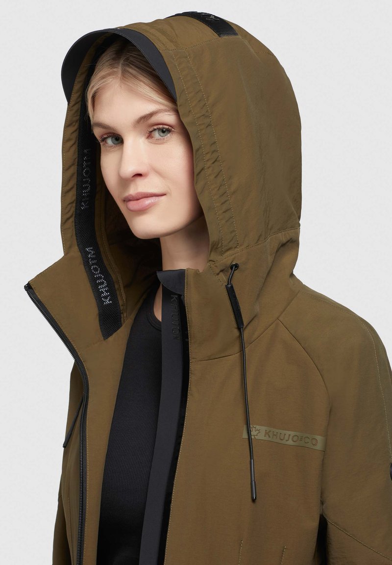 Olivgrün Kapuzenjacke mit einem Reißverschluss vorne, schwarzer Akzentuierung und verstellbaren Kordeln. Logo auf der Brust angebracht. Strukturierter Stoff.