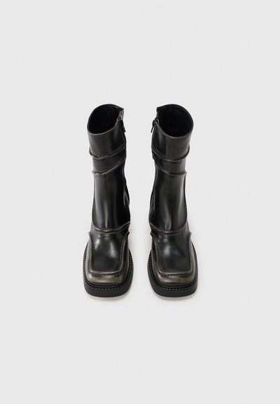 Μαύρα δερμάτινα μποτάκια αστραγάλου με τετράγωνη μύτη, υφή στην επάνω επιφάνεια και εμφανείς ραφές. Πλαϊνά φερμουάρ και λείο τελείωμα συμπληρώνουν το σχέδιο.