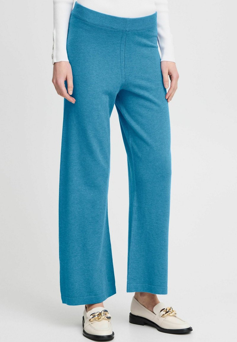 Vaaleansiniset leveälahkeiset housut, jotka on valmistettu pehmeästä kankaasta ja joissa on mukava elastinen vyötärönauha. Yhdistetty valkoisiin loafer-kenkiin.