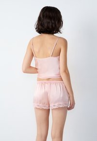 Pinke Satin-Camisole mit Spaghetti-Trägern, kombiniert mit passenden Shorts, die einen Spitzenbesatz am Saum haben. Weiche Textur und glatte Oberfläche.