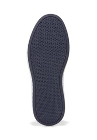 Guma spodní část boty s texturovaným vzorem a značkou "Cole Haan" v oblasti paty, vystavená na bílém pozadí.