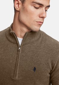 Pulover tricotat cu nervuri maro, cu un guler cu fermoar, având un logo bleu închis pe piept, material texturat și un design ajustat.