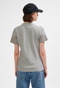 Grå pikétröja med korta raglanärmar och krage. Kombinerad med blå jeans. Svart keps bärs bakåtvänd, med synliga örhängen.