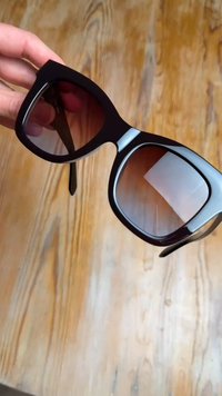 Sunglasses featuring large, dark lenses, black frames with a glossy finish, and silver accents at the hinges. Textured arms enhance grip.