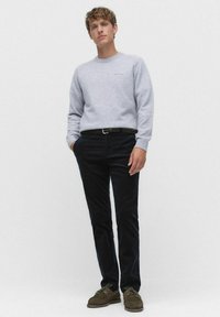 Ljusgrå tröja med rund krage, mörkblå byxor och bruna mockaskor. Enkelt design med en subtil logotypdetalj på tröjan.