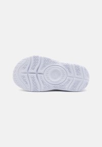 Semelle de sneaker blanche avec un motif de traction ondulé, un détail de logo circulaire au centre et une texture lisse, semblable au caoutchouc, sur l'ensemble.
