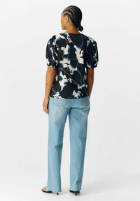 Blusa negra con mangas abullonadas con un patrón abstracto en azul y blanco, combinada con jeans rectos de color azul claro.