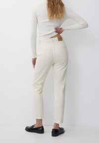 Jeans blancs taille haute, coupe droite, avec cinq poches et une étiquette en tissu rectangulaire sur la taille. Texture lisse et unie, longueur cheville.