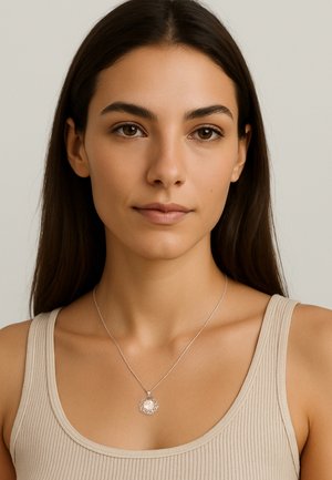 Collana d'argento con un pendente decorativo caratterizzato da un intricato design in filigrana, indossata da un modello con lunghi capelli scuri e una maglietta beige.