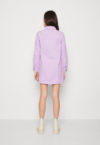 Lavendelfarbenes Denimkleid mit langen Ärmeln und Kragen. Hat einen geraden Schnitt und geknöpfte Manschetten, kombiniert mit hellen Plateaustiefeln.