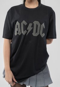 Black t-shirt made of cotton, featuring large gray AC/DC logo and lightning bolt. Paired with a checkered black and white pleated skirt.
