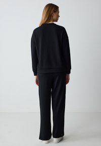 Black sweatshirt and matching pants made of a soft, textured fabric. The outfit features a relaxed fit and is paired with white sneakers.