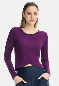 Purple long-sleeve crop top with a round neckline and a twisted front design. Made of smooth fabric, paired with navy high-waisted pants.