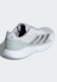 Biela športová obuv s textúrovaným sieťovaným zvrškom, sivými syntetickými doplnkami, troma sivými pruhmi a vzorovanou gumovou podrážkou.