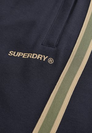 Navyblauwe sweatshirt met een gouden "SUPERDRY" logo, met een gestructureerde groene en beige strookdetail aan één zijde. Zacht materiaal.