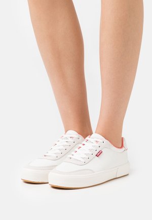 White sneakers with a textured leather and suede upper, red accents on the heel and laces, and a rubber sole. Single logo tag on side.