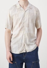 Kortærmet skjorte i lys beige med paisley mønster, lavet af glat stof. Frontknapper og detaljer med camp krave.