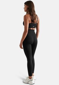 Top sportivo nero a coste e leggings a vita alta, con design senza cuciture e dettagli con aperture. Indossati con scarpe da ginnastica bianche.