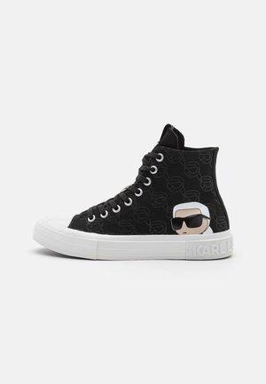 Czarny wysokiej klasy sneaker z białą podeszwą, z stylizowaną twarzą w okularach przeciwsłonecznych po boku i powtarzającym się wzorem twarzy na tkaninie.