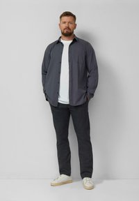 Szara koszula noszona na białej koszulce, w zestawieniu z ciemnymi spodniami i białymi trampkami. Charakteryzuje się fasonem zapiętym na guziki oraz bocznymi kieszeniami.