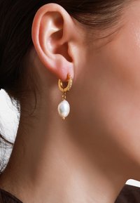Des boucles d'oreilles en or en forme de cercle présentent un accent étincelant, avec une perle blanche de forme irrégulière suspendue en bas. Fini métallique lisse, design élégant.