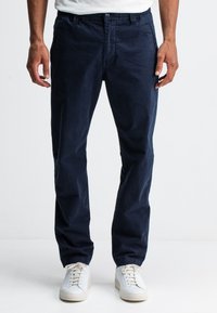Marineblauwe chino's van katoen, met een klassieke snit, zijzakken en een gladde textuur, gecombineerd met witte sneakers.