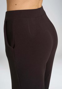 Pantaloni marroni elasticizzati con una vita alta, dotati di tasche laterali e una vestibilità sagomata che si adatta alla forma del corpo.