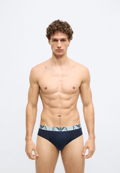 Cuecas masculinas azul-marinho com um cós elástico azul claro com um logótipo. O tecido parece liso, com um corte ajustado e costuras mínimas.