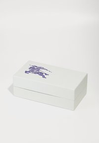 Caja rectangular blanca con tapa abatible, que presenta una detallada ilustración púrpura de un jinete en la parte superior. Textura suave, diseño minimalista.