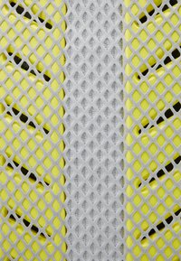 Tissu en maille flexible en jaune et gris, présentant un motif en forme de losange, avec des textures superposées et des matériaux sous-jacents visibles.