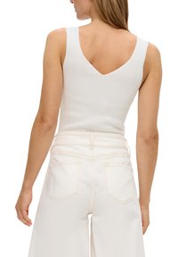 Weißes geripptes Tanktop mit V-förmigem Rücken, kombiniert mit hochgeschnittenen weißen Jeans, die zwei Taschen haben, eine glatte Textur und robuste Nähte aufweisen.
