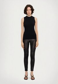 Black ribbed sleeveless top paired with black leggings featuring a textured, shiny pattern, finished with black strappy sandals.